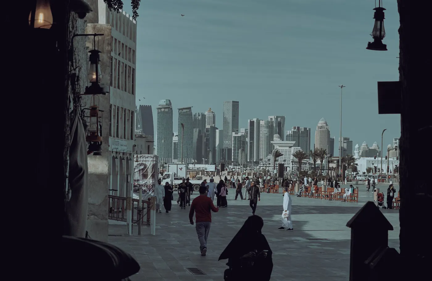 People walking across a square towards Doha’s skyline, seen through a dark historic archway