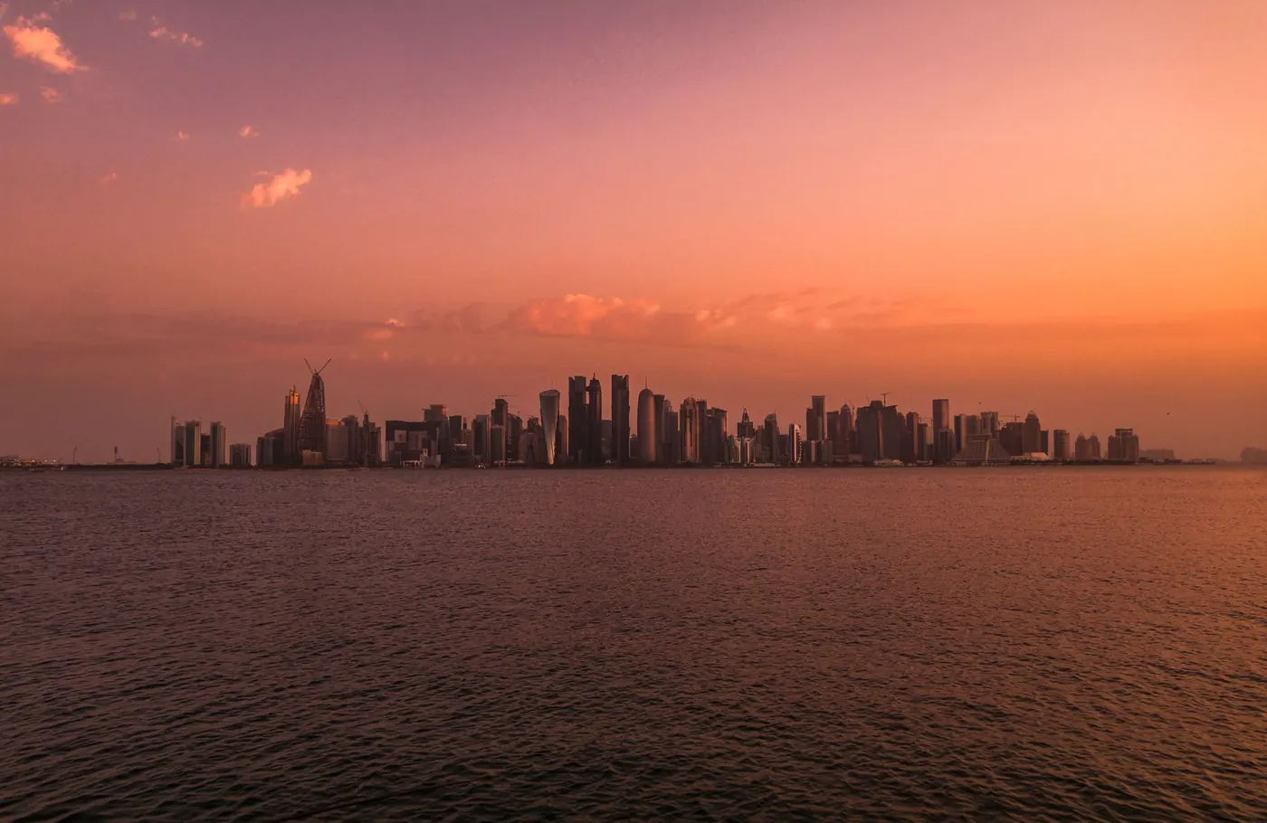 The Doha skyline low on the horizon under an orange sunset sky