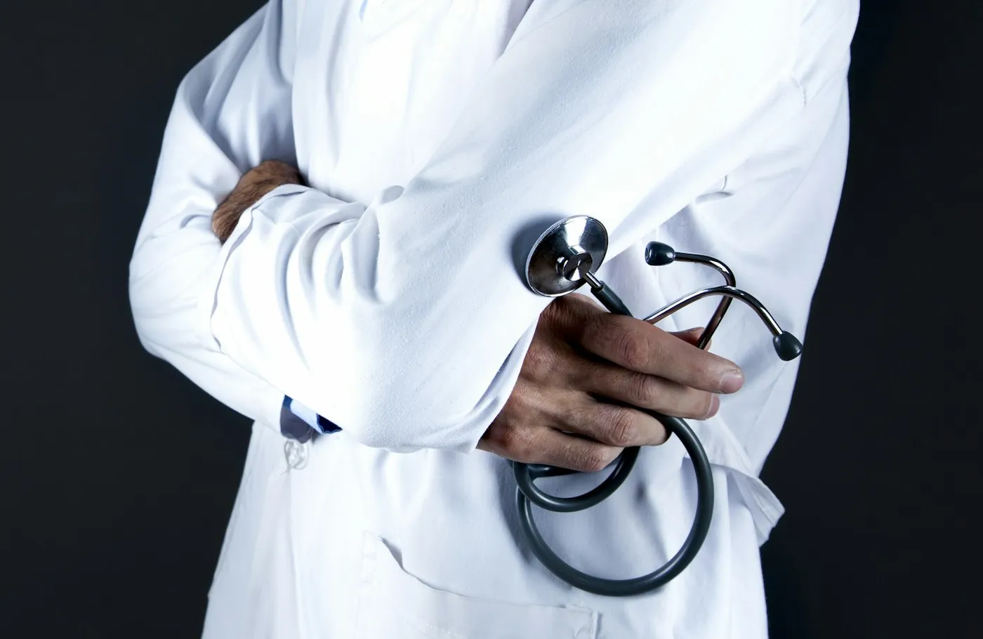 A clinician in a white coat, arms folded, holding a stethoscope against a dark background