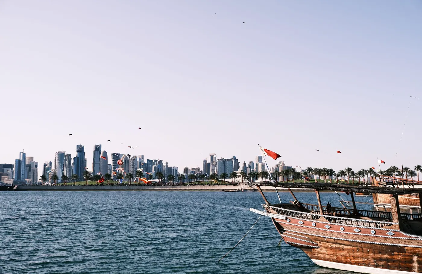 A wooden dhow flying Qatari flags in the harbour, with the Doha skyline across the water