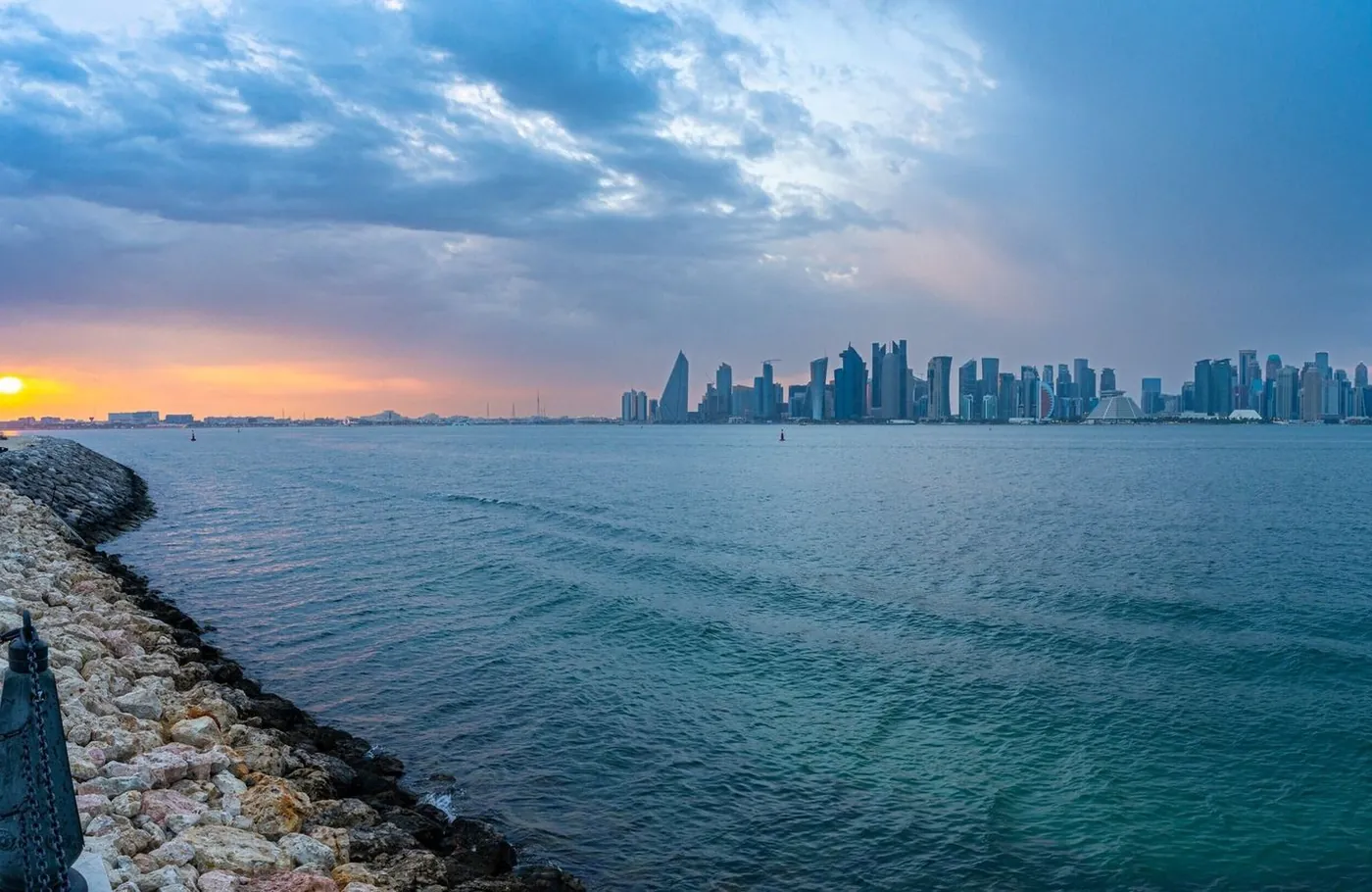Doha’s skyline across the water at sunset, with the Corniche shoreline in the foreground