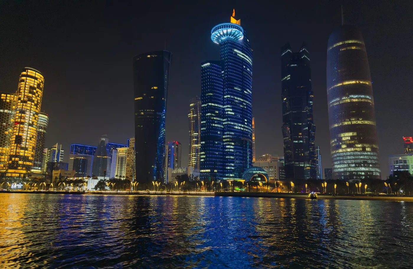 West Bay towers lit up at night, reflected in the water of Doha Bay